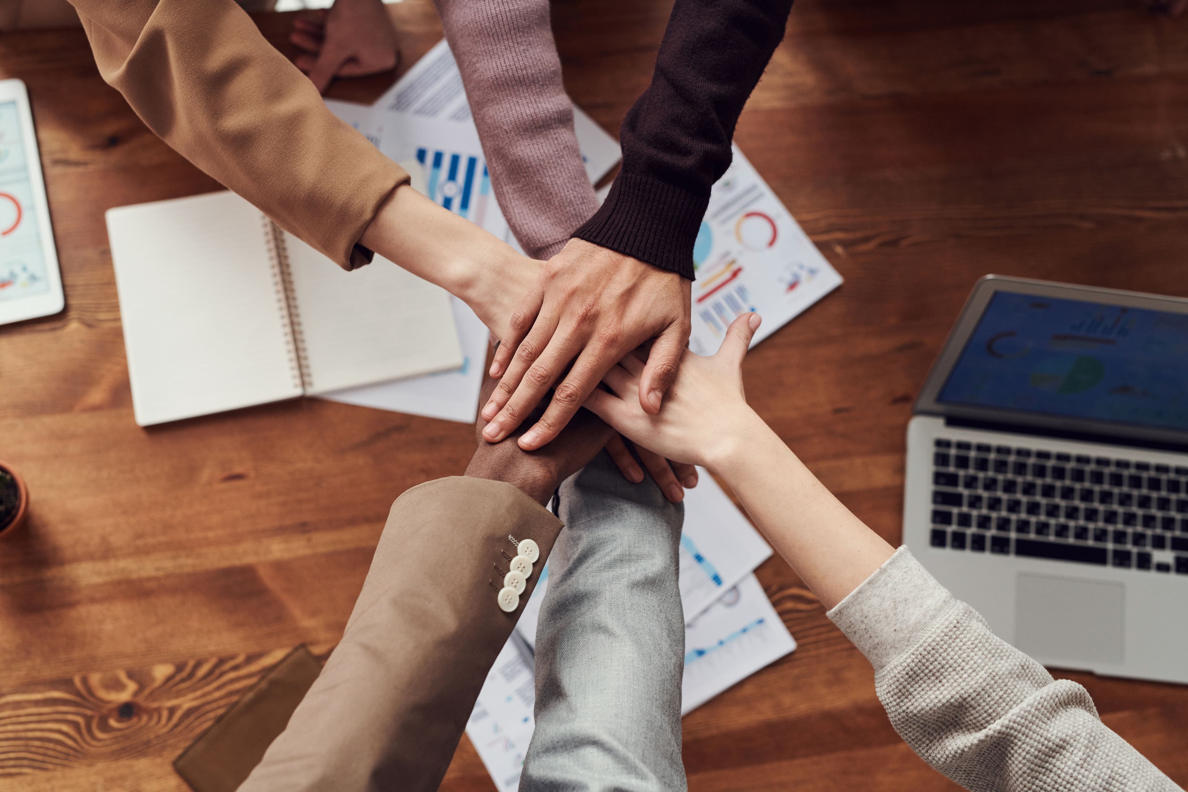 Team members joining hands over a desk with charts and a laptop